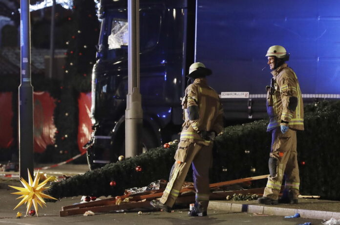 Firefighters look at a toppled Christmas tree after a truck ran into a crowded Christmas market and killed several people in Berlin, Germany, Monday, Dec. 19, 2016. Photo: Michael Sohn / Associated Press