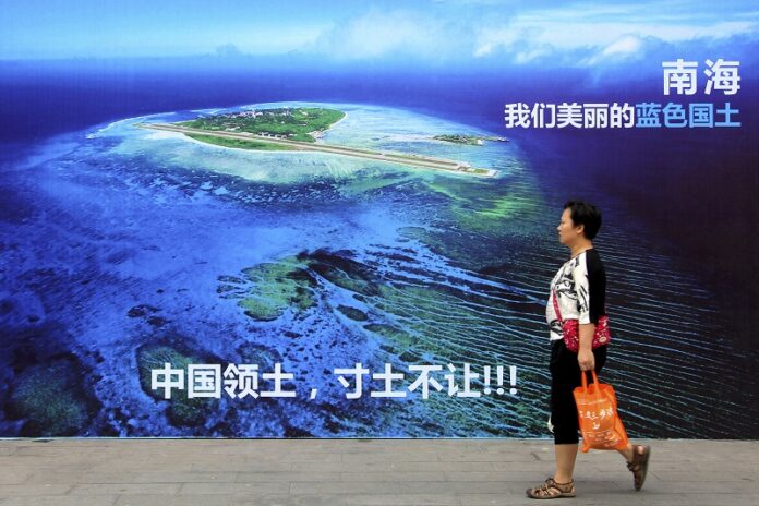 A woman walks past a billboard featuring an image of an island in South China Sea on display with Chinese words that read: