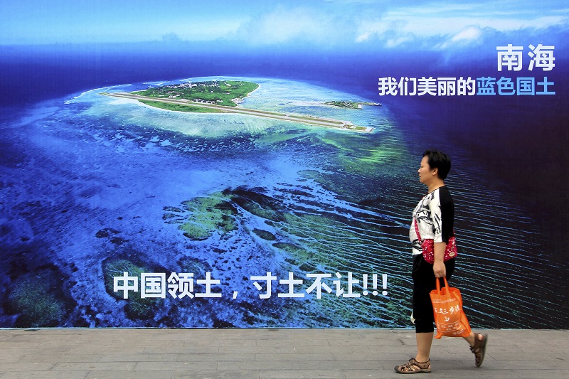 A woman walks past a billboard featuring an image of an island in South China Sea on display with Chinese words that read: