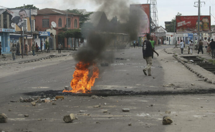 People walk near burning debris during protests in Kinshasa, Democratic Republic of Congo, Tuesday. Photo: John Bompengo / AP.
