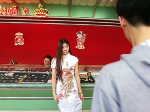 A young woman trying on Chinese dress for male friend to take a photo.