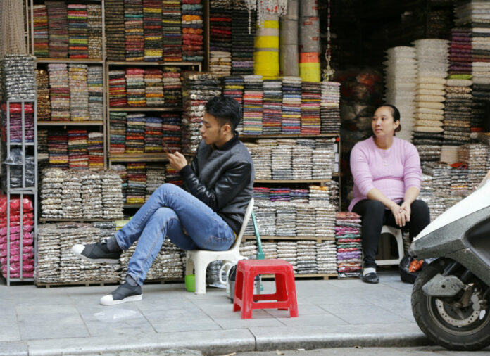 A man and a woman waiting waiting for customers at their tailor accessories shops in Hanoi, Vietnam, Dec. 1. Photo: Tran Van Minh / AP.
