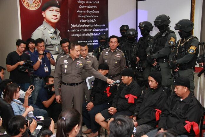 Then-police chief Somyot Pumpanmuang hands a microphone on Sept. 11, 2014, to four of five people accused of being ‘Men in Black’ militants during 2010 political unrest in Bangkok.