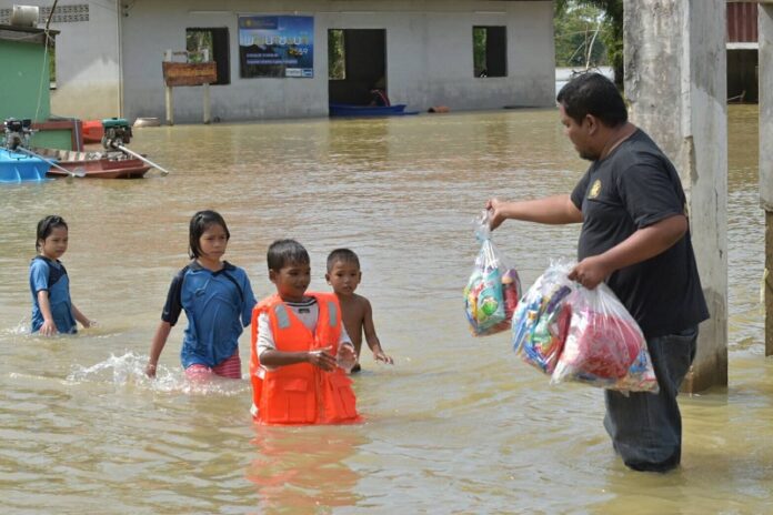 Children walk through a flooded community to receive donated foodstuffs Monday in Surat Thani province.