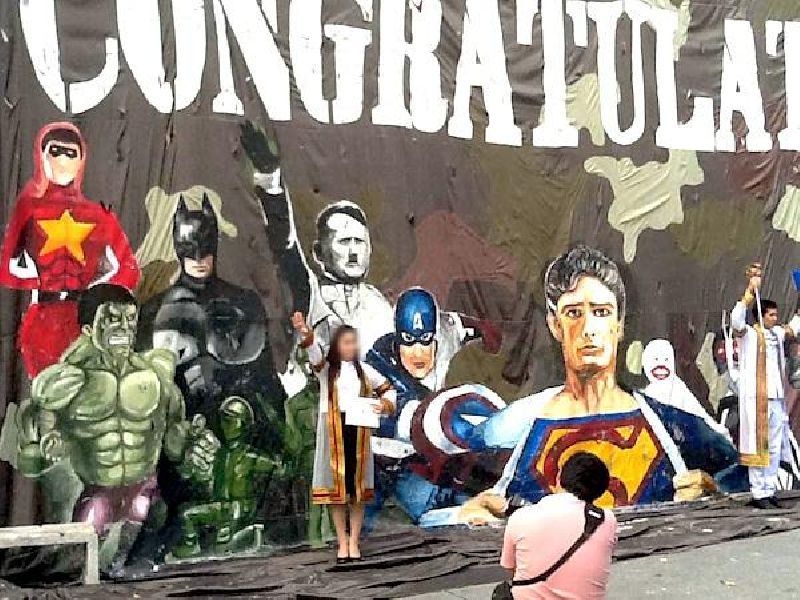 A graduating student poses for a photo before a mural of superheroes including Adolf Hitler set up at Chulalongkorn University in July 2015 to mark graduation ceremonies.