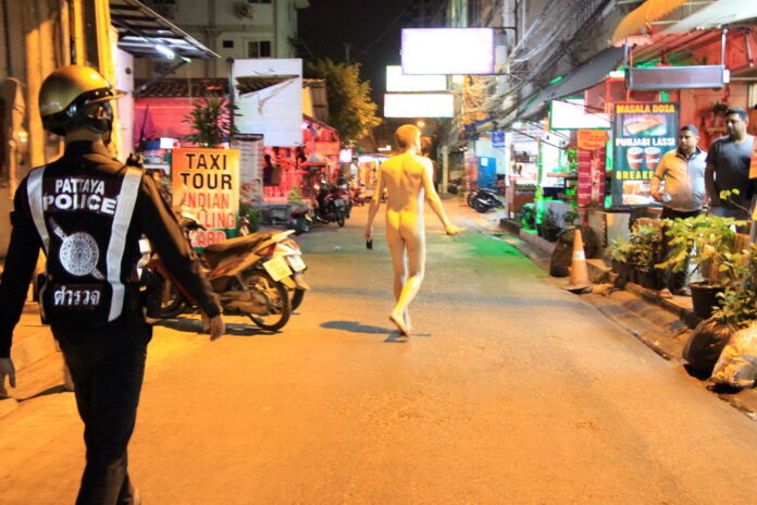 A Police officer trails an agitated man with a knife menacing people Wednesday night in downtown Pattaya city.
