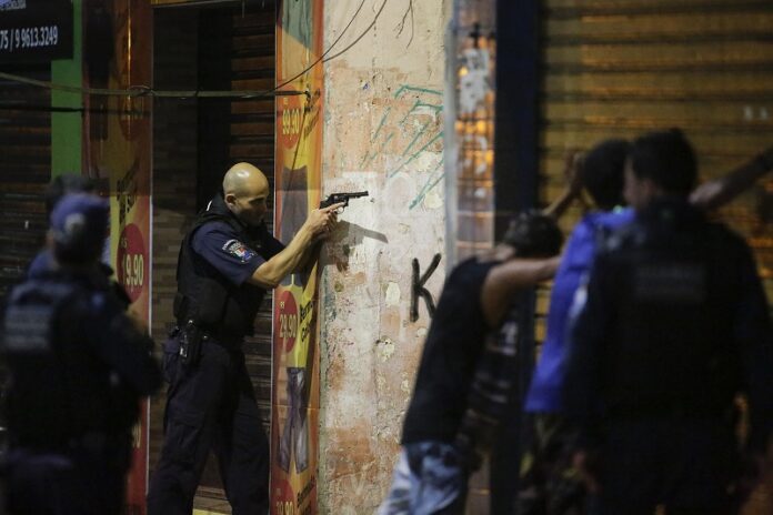 A municipal guard aims his weapon as two men are searched Tuesday in Vitoria, Espirito Santo state, Brazil. Photo: Diego Herculano / Associated Press