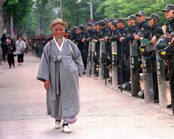 An elderly man wearing traditional Korean costumes walks past a police line as workers stage an anti-government rally calling for job security in 1998, at Chongmyo Park in Seoul, South Korea. Photo: Ahn Young-joonm / Associated Press