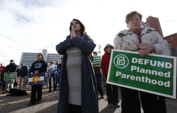 Participants in an anti-abortion rally hold signs and pray as they listen to a member of Christian clergy read from the Bible, in front of Planned Parenthood of the Rocky Mountains, in Denver, Feb. 11, 2017. (AP Photo/Brennan Linsley)