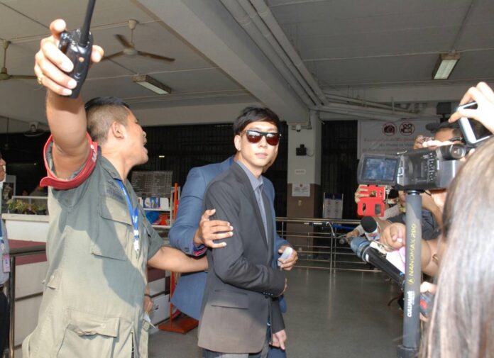 Akarakit Worarojcharoendet, in suit, is escorted away from the court Monday afternoon after freed on bail.