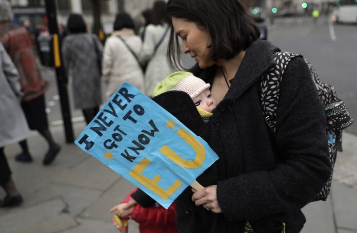 A woman carries a baby and holds a banner as she takes part in a protest Wednesday outside the House of Commons in central London. Photo: Matt Dunham / Associated Press