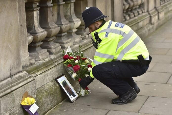 A police officer on Thursday places flowers and a photo of fellow police officer Keith Palmer, who was killed in yesterdays attack, on Whitehall near the Houses of Parliament in London. Photo: Dominic Lipinski / Associated Press