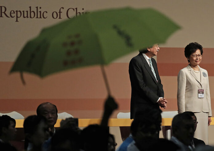 A protester raises an umbrella to protest former Hong Kong Chief Secretary Carrie Lam, right, after she declared her victory in the chief executive election while standing with former Financial Secretary John Tsang on Sunday. Photo: Vincent Yu / Associated Press