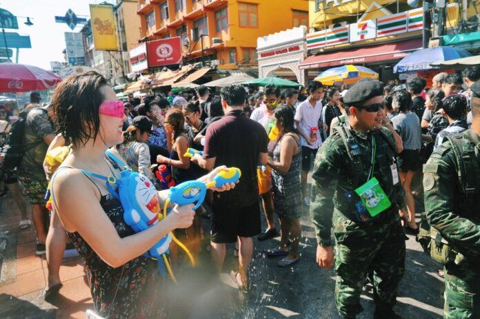 A woman with a Doraemon water gun backpack sprays soldiers during 2017 Songkran celebrations on Khaosan Road.