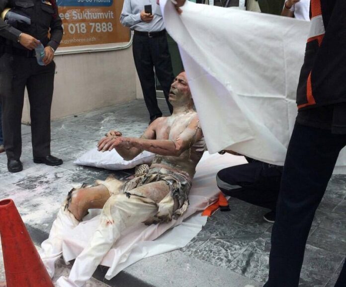 A badly burned man sits on the sidewalk Friday afternoon in front of the Iranian Embassy in Bangkok.