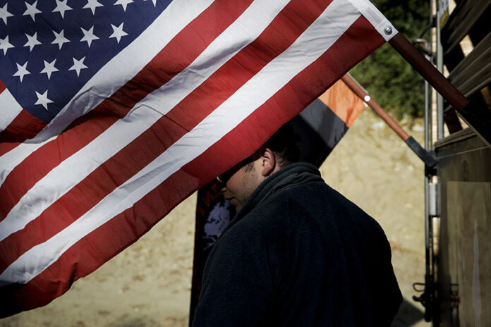 Iraq war veteran Colt Romberger pauses behind an American flag hanging from his trailer in 2017 in Santa Clarita, California. Photo: Jae C. Hong / Associated Press