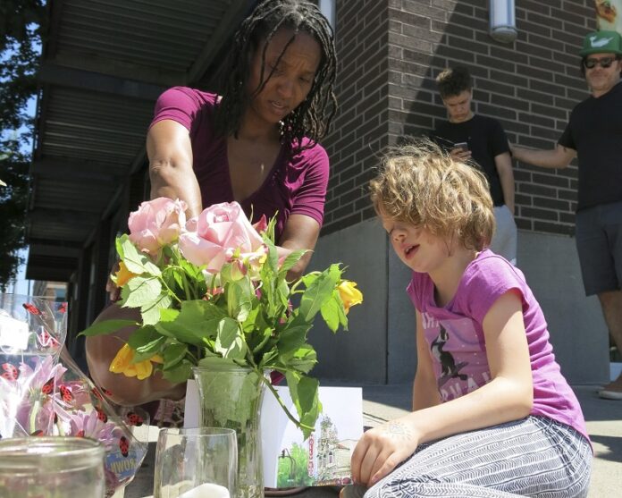 Angel Sauls, at left, helps her stepdaughter, Coco Douglas arrange a sign and some painted rocks she made for a memorial in Portland, Oregon, on Saturday for two bystanders stabbed to death Friday while trying to stop a man who was yelling anti-Muslim slurs and acting aggressively toward two young women. Photo: Gillian Flaccus / Associated Press
