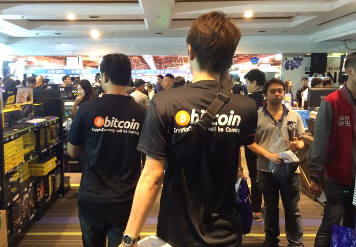 Two men wearing Bitcoin shirts stroll through the Commart expo in Bangkok on Thursday