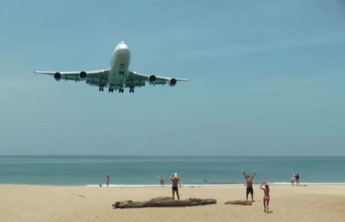 Tourists pose for photos as a jet approaches on March 21, 2016, at Phuket’s Mai Khao Beach.