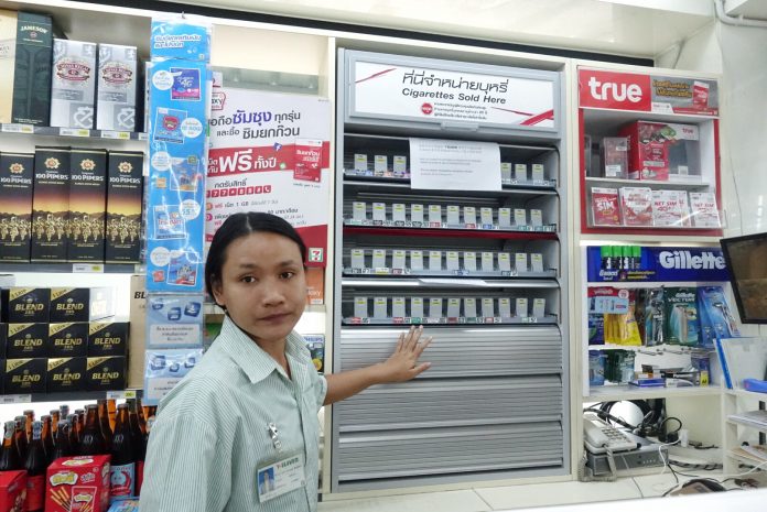 A 7-Eleven employee opens four shelves of metallic covers over cigarette shelves in a convenience store branch Tuesday in Bangkok.