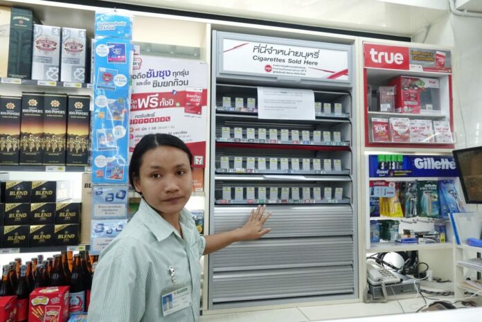 A 7-Eleven employee opens four shelves of metallic covers over cigarette shelves in a convenience store branch Tuesday in Bangkok.