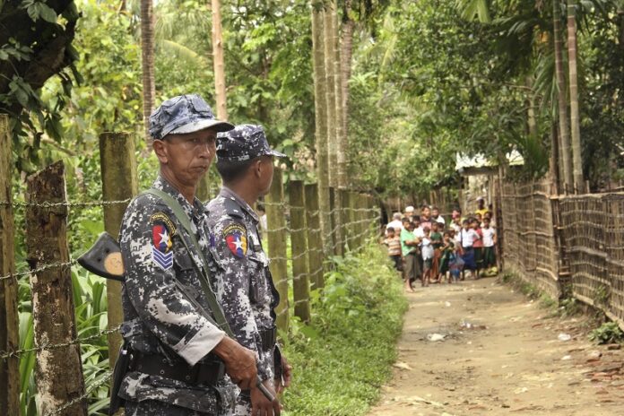 Myanmar's Border Guard Police officers stand guard at a village street July 13 as some residents stand together in Yinmar Chaung Taung village of northern Buthidaung township where the majority Rohingya Muslims and some Rakhine Buddhists live in Rakhine state, Myanmar. Photo: Esther Htusan / Associated Press