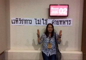 Pakavadi Veerapasapong makes three-finger salutes associated with opposing the military regime at an academic forum before a banner asserting the event 'is not a military barracks' earlier this month in Chiang Mai. Photo: Pakavadi Veerapasapong / Facebook