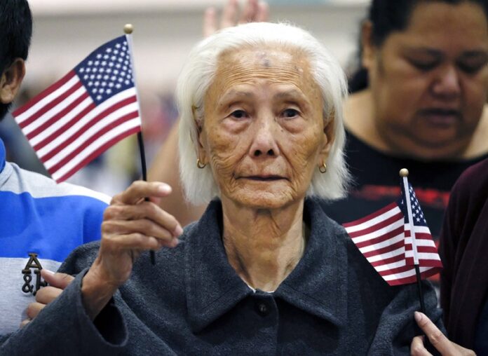 Hong Inh waves an American flag Tuesday as she takes the oath to become a United States citizen at the Los Angeles Convention Center. Photo: Richard Vogel / Associated Press