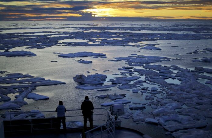 Researchers look out from the Finnish icebreaker MSV Nordica on July 21, 2017, as the sun sets over sea ice floating on the Victoria Strait along the Northwest Passage in the Canadian Arctic Archipelago. Photo: David Goldman / Associated Press