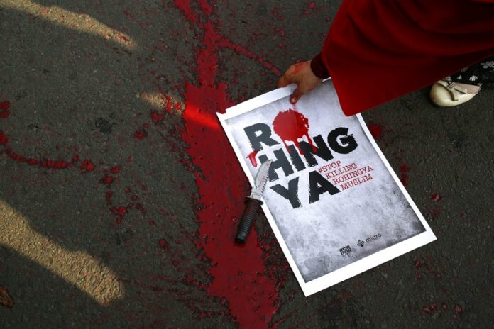 A Muslim protester picks up a poster as fake blood is seen spattered on the ground after a theatrical act depicting the violence against Muslim Rohingya in western Myanmar performed during a rally on Sunday, Sept. 3, 2017 in Jakarta, Indonesia. Photo: Dita Alangkara / Associated Press