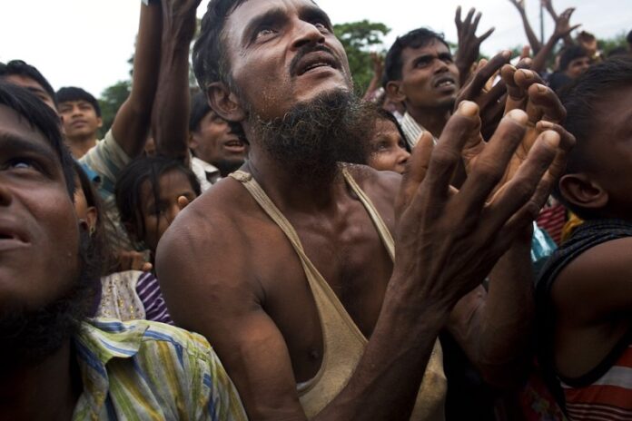 A Rohingya man stretches his arms out for food distributed by local volunteers, with bags of puffed rice stuffed into his vest in 2017 at Kutupalong, Bangladesh. Photo: Bernat Armangue / Associated Press