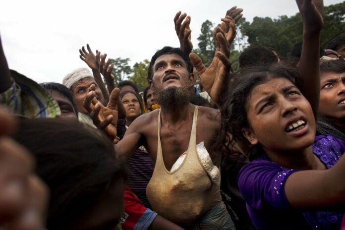 A Rohingya man stretches his arms out for food distributed by local volunteers, with bags of puffed rice stuffed into his vest on Sept. 9 at Kutupalong, Bangladesh. Photo: Bernat Armangue / Associated Press