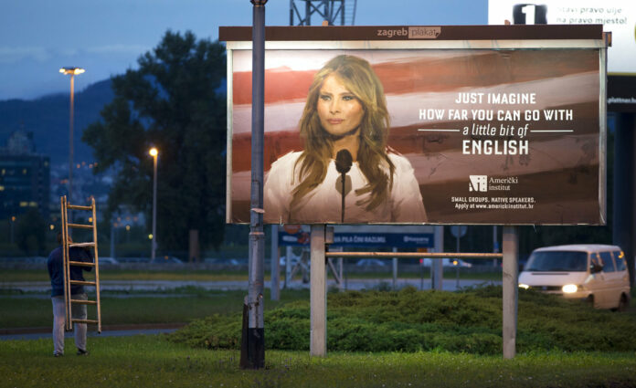 A worker carries a ladder walks past a billboard depicting the first lady Melania Trump that advertises a language school Friday in Zagreb, Croatia. Photo: Darko Bandic / Associated Press