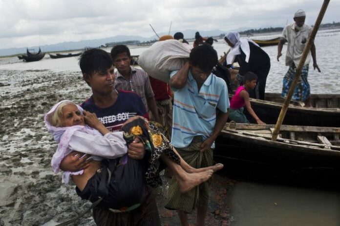 A Rohingya ethnic minority from Myanmar carries an elderly woman as they alight from a local boat on which they crossed a river, after crossing over to the Bangladesh side of the border Sept. 1 near Cox's Bazar's Dakhinpara area. Photo: Bernat Armangue / Associated Press