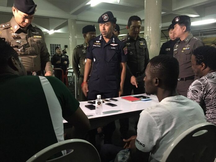 Head of the 191 emergency response unit Surachet Hakpan, in blue, looks over the documents of foreigners arrested early Monday in a raid targeting black foreigners in Bangkok.