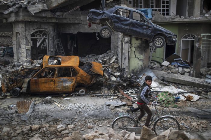 A boy rides his bike past destroyed cars and houses in a neighborhood recently liberated by Iraqi security forces, on the western side of Mosul, Iraq, on March 19, 2017. Photo: Felipe Dana / Associated Press