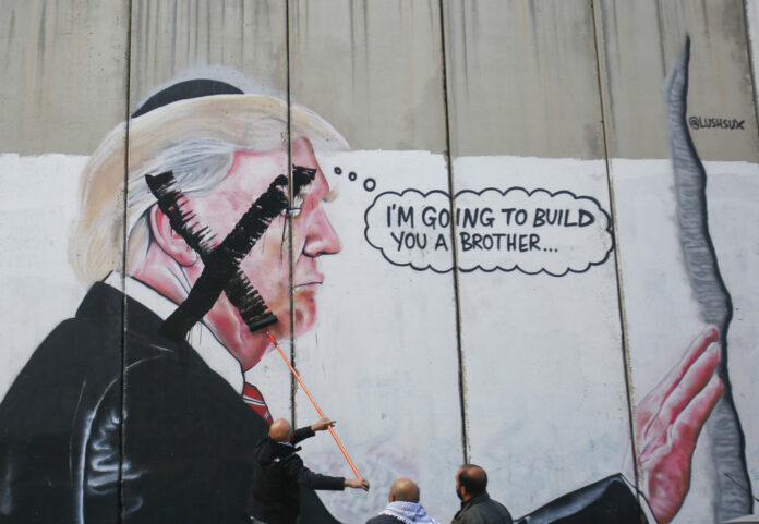 A Palestinian paints over a mural of the U.S. President Donald Trump during a protest in Bethlehem, West Bank on Thursday. Photo: Nasser Shiyoukhi / Associated Press