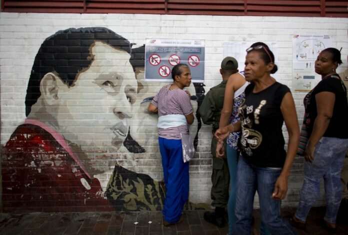 People search for their names on voter lists for mayoral elections by a mural of Venezuela's late President Hugo Chavez at a school serving as a polling station in 2017 in Caracas, Venezuela. Photo: Ariana Cubillos / Associated Press