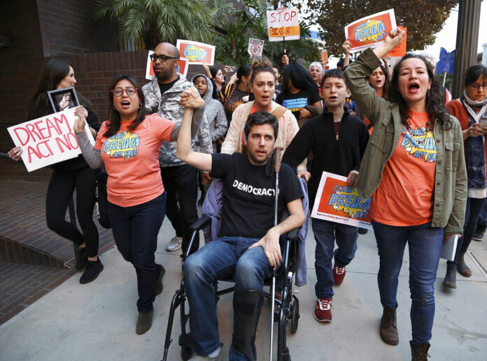 Cristina Jiminez, left, and Ady Barkan, in wheelchair, lead a small delegation to the office of California Democratic Sen. Dianne Feinstein, urging the Democrats to protect the Deferred Action for Childhood Arrivals (DACA) program in Los Angeles, Wednesday, Jan. 3, 2018. Photo: Reed Saxon / Associated Press