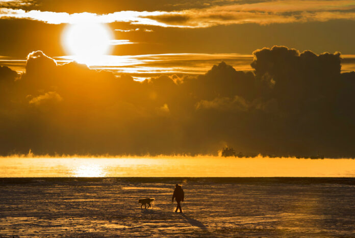 A man walks his dog across the snow-covered beach while a cargo ship sits in the steaming fog of Lake Ontario in Toronto. According to a report released on Thursday, Jan. 18, 2018, U.S. and British scientists calculate that 2017 wasn’t the hottest year on record, but close and unusually warm for no El Nino cooking the books. Photo: Frank Gunn / The Canadian Press