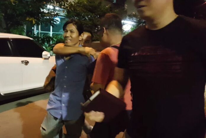 Kritchapon Poonsilpa is led away from his residence by police officers Monday night.