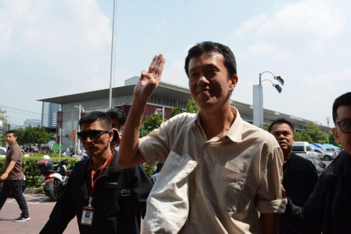 Ekachai Hongkanwan flashes a three-finger salute of the junta opposition in front of the Pathum Wan Police Station on Saturday.