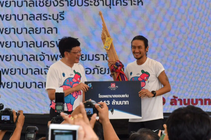 Artiwara ‘Toon Bodyslam’ Kongmalai holds a ‘kaen’ while handing a 143 million baht check to a Khon Kaen Hospital official.