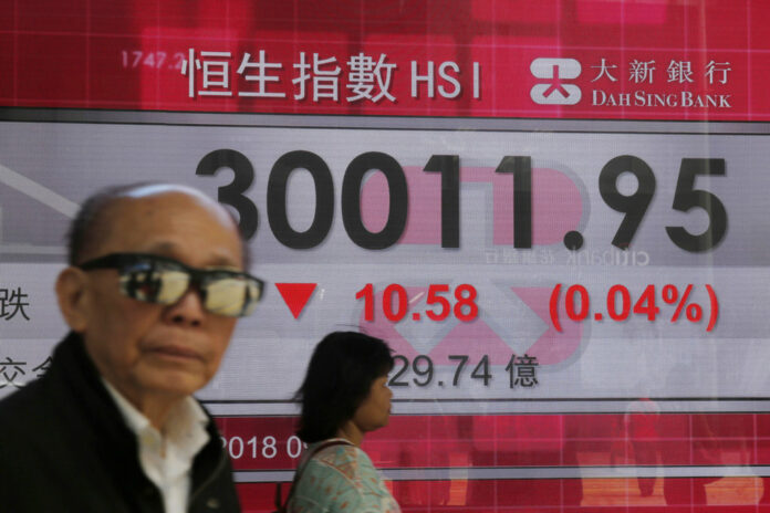 People walk past an electronic board showing Hong Kong share index outside a local bank in Hong Kong on Thursday. Photo: Kin Cheung / Associated Press