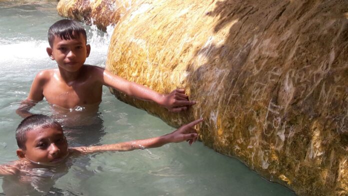 Children point Monday to marks left by guests on the edge of Emerald Pool in Krabi province. Photo: Matichon