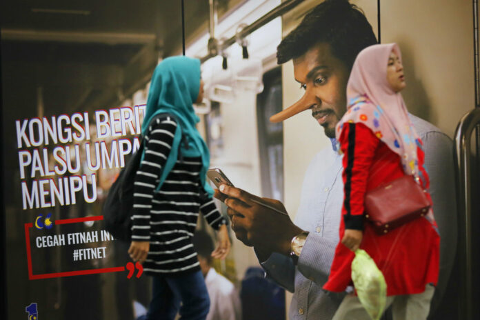Commuters walk past an advertisement discouraging the dissemination of fake news, which reads