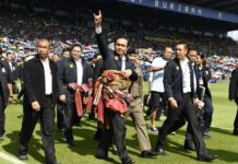 Watching Prayuth and ‘Three Friends’ Campaign No Fun for Others Junta chairman Prayuth Chan-ocha waves to the crowd at Thunder Castle Stadium in Buriram province on May 7. Newin Chidchob, in shorts, walks close to him just behind.