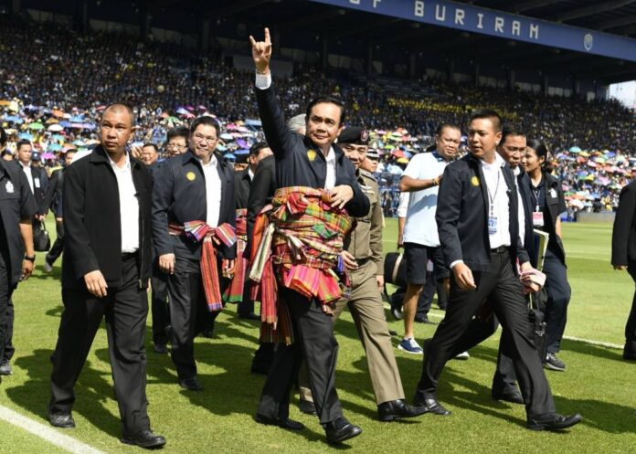 Junta chairman Prayuth Chan-ocha waves to the crowd at Thunder Castle Stadium in Buriram province on May 7. Newin Chidchob, in shorts, walks close to him just behind.