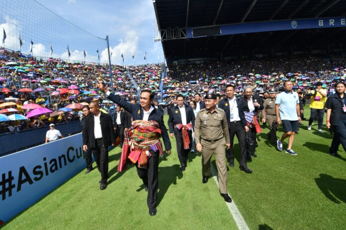 Junta chairman Prayuth Chan-ocha waves to the crowd at Thunder Castle Stadium in Buriram province yesterday. Newin Chidchob, in shorts, walks close to him just behind.