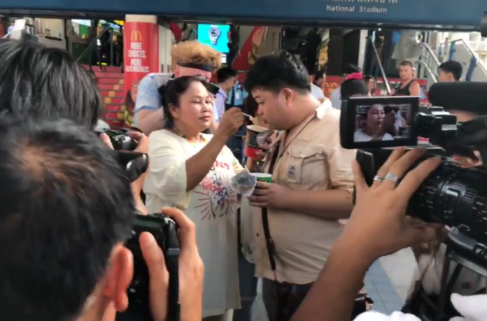 A woman feeds Thammasat student activist Parit “Penguin” Chiwarak with instant noodle on a BTS skywalk Monday. Image: Nuttaa Mahattana / Facebook